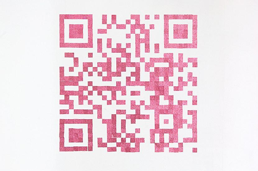 You see a white wall on which is constructed a QR-code. The squares that constitute the code are pink and glittery, made from some thick adhesive pasted to the wall.
