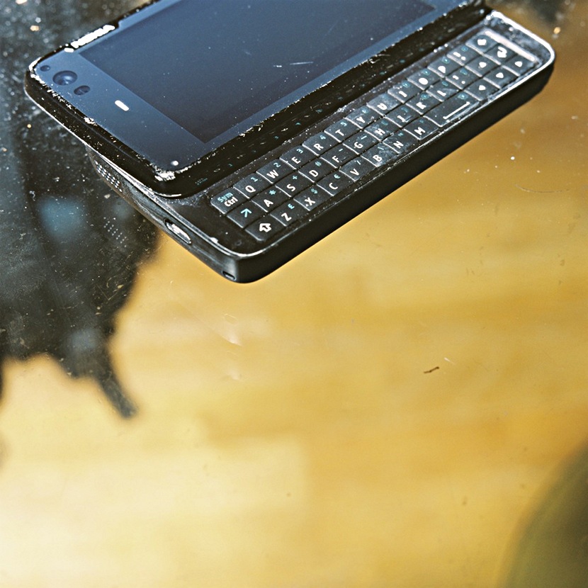 In the upper part of the screen you see a smartphone. A landscape format screen with a keyboard slid out underneath. The screen is scratched and there are stains of white paint all over the device. The phone appears to be floating.
